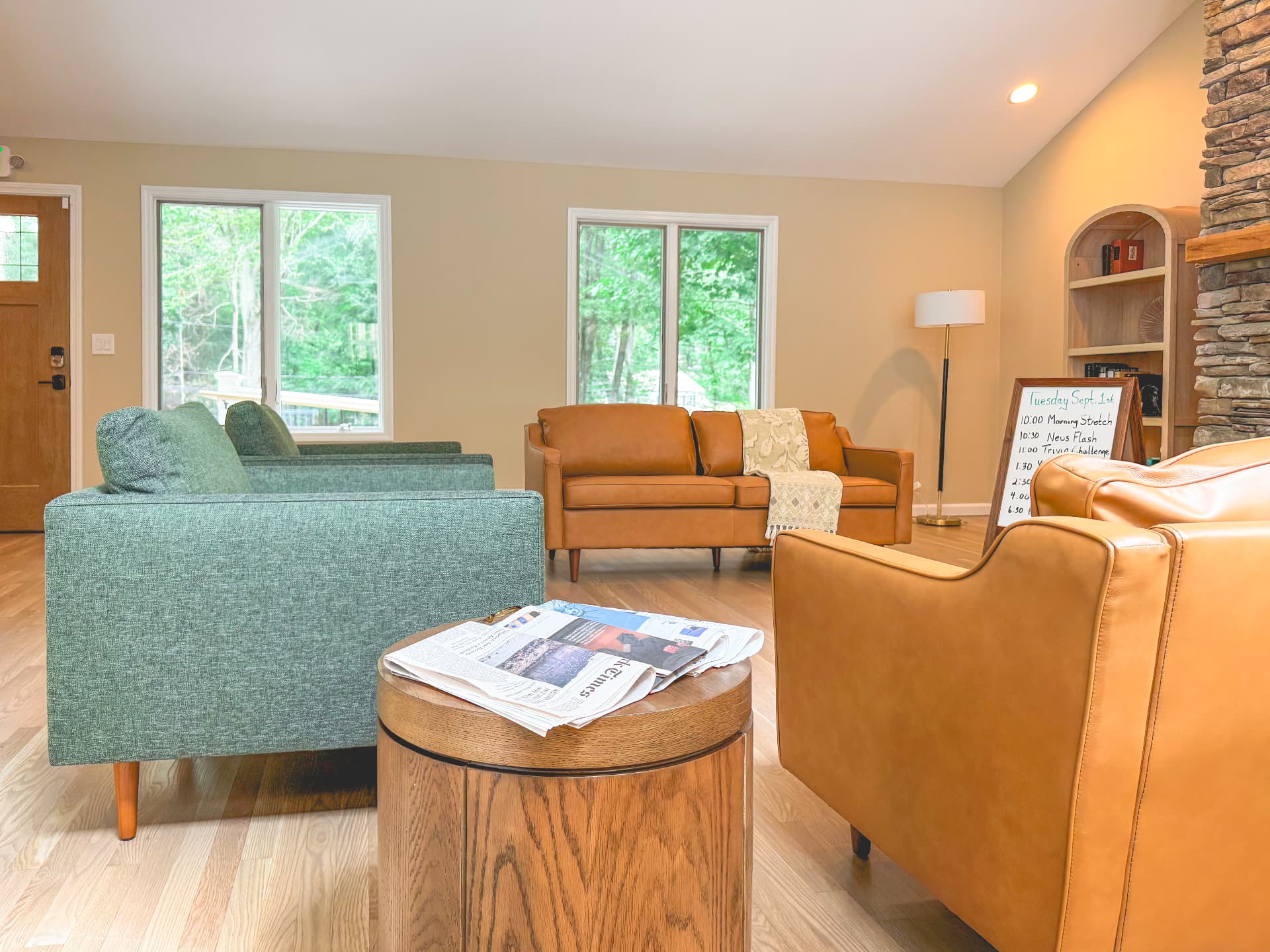 Living room with green and leather sofas, stone fireplace and woodland views