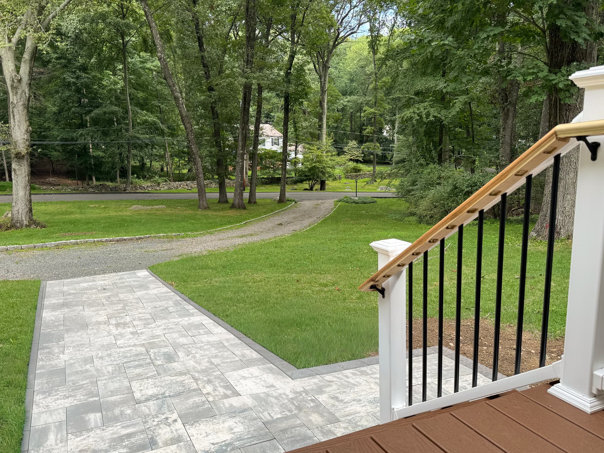 Front porch overlooking a paved walkway, lawn and mature trees